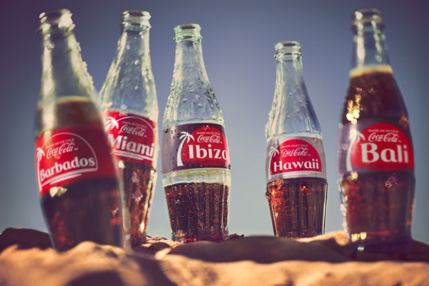 Bottles of coke on the beach with labels showing holiday destinations
