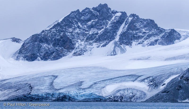 An icy mountain protrudes from a large glacier ice sheet by the sea
