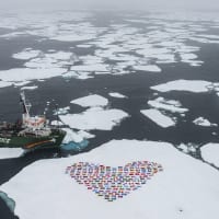 A Greenpeace ship alongside and ice floe that's covered in the flags of the world arranged in a heart shape.