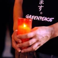 Hands holding a candle in a jar. The holder is wearing a black Greenpeace t-shirt.
