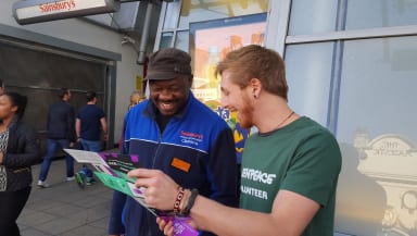 An activist speaks to a worker in a Sainsbury's uniform, showing them a leaflet. They're both smiling.