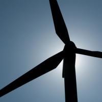 The sun creates a silhouette behind a wind turbine. Wind power is one of the most common forms of renewable energy.