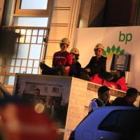 Three people sit on top of a box outside BP headquarters in London.