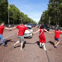 Protesters in red hold hands and dance across a road to block traffic and declare a climate emergency