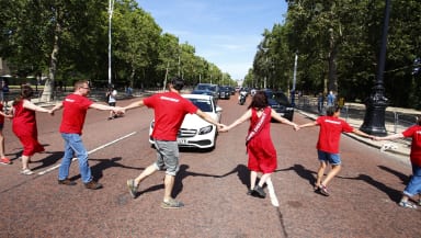 Protesters in red hold hands and dance across a road to block traffic and declare a climate emergency