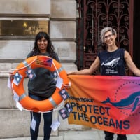 People in Greenpeace t-shirts outside the Foreign and Commonwealth Office hold a banner saying Protect the Oceans, and a rescue ring decorated with postcards.