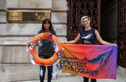People in Greenpeace t-shirts outside the Foreign and Commonwealth Office hold a banner saying Protect the Oceans, and a rescue ring decorated with postcards.