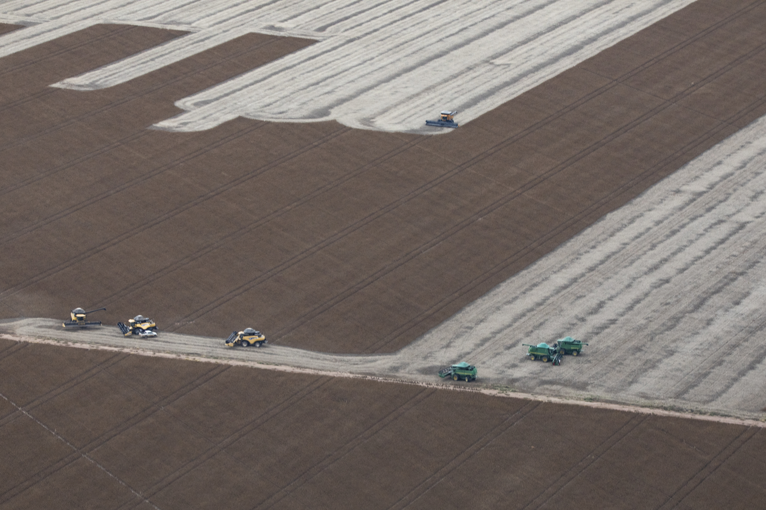 Aerial view of industrial farming machines working in a vast brown field of crops.