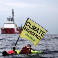 Swimmer in front of an oil rig with a banner that says "Climate emergency"