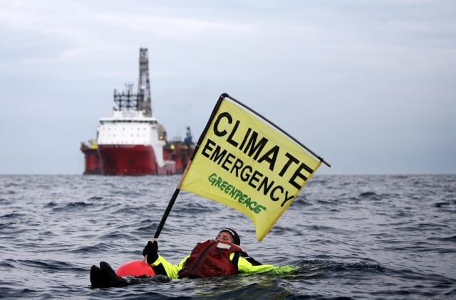 Swimmer in front of an oil rig with a banner that says "Climate emergency"