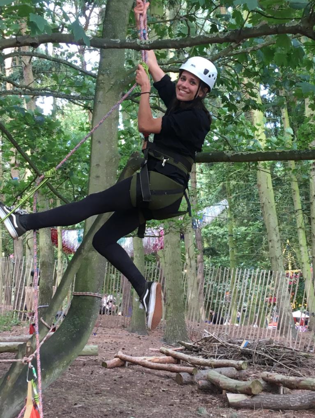 A woman in a helmet and a harness smiles into the camera as she rides a zipline.