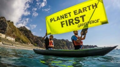 Two activists in a kayak hold a large banner reading 'Planet Earth first'.