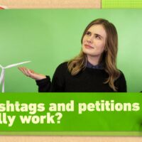 Video presenter Lex Croucher (long hair, black sweater) looks up with a puzzled expression and open-palm gesture against a green background. Text reads 'Do hashtags and petitions actually work?'