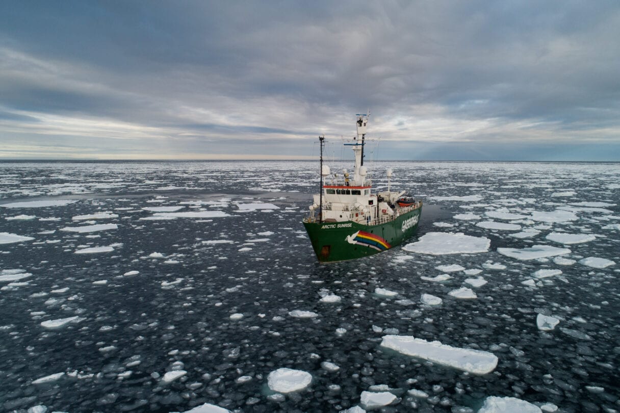 Aerial photo of a green shop in a dark ocean with chunks of ice floating on the surface.