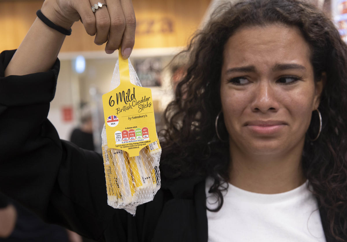 A woman holds up a plastic pouch of individually-wrapped cheese sticks. She does not look pleased.