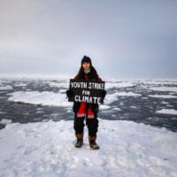 Mya-Rose Craig standing on an ice floe holding a sign reading 'Youth strike for climate'