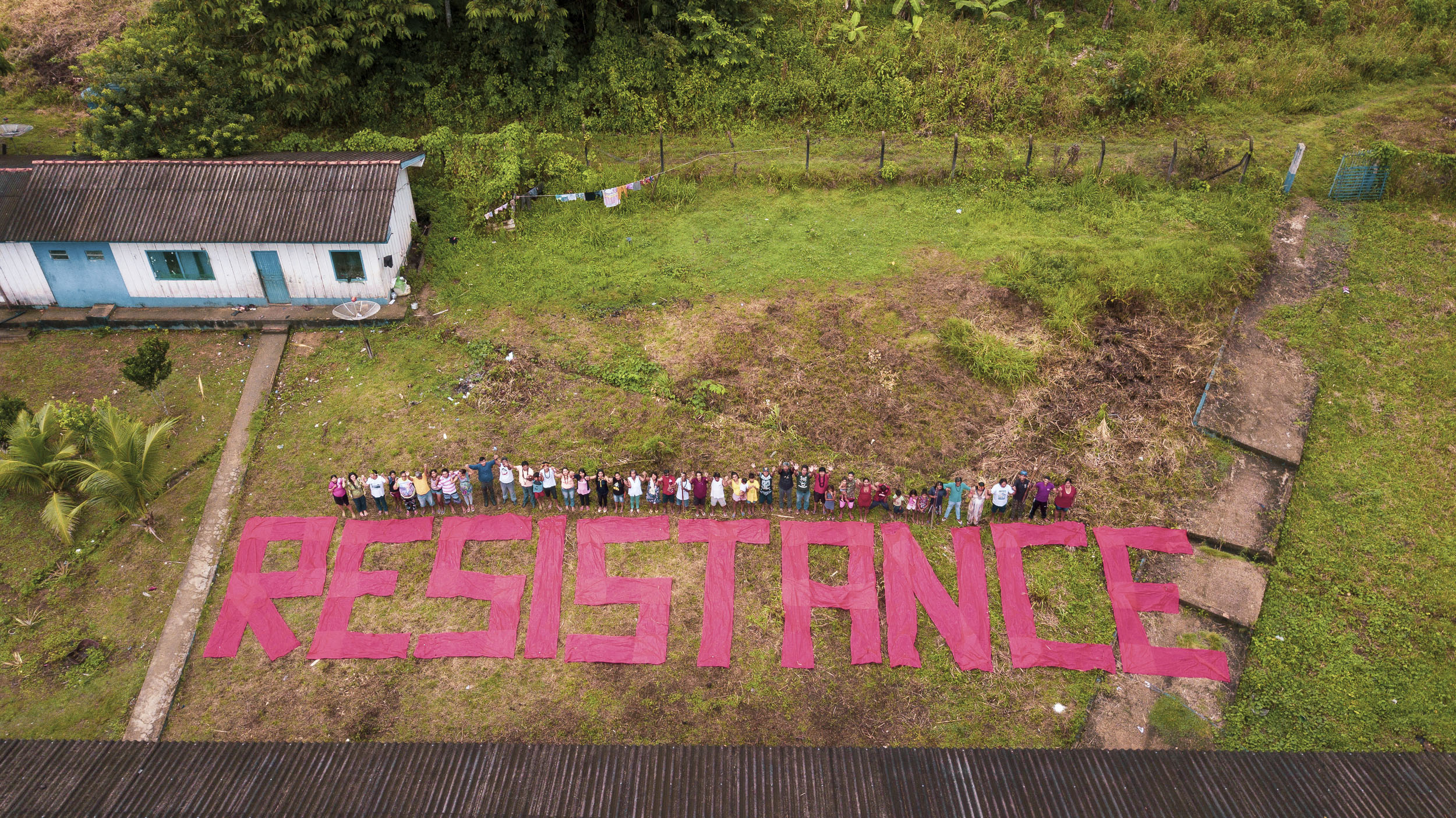 An aerial view of the Karipuna standing over a banner written on the ground reading RESISTANCE. 