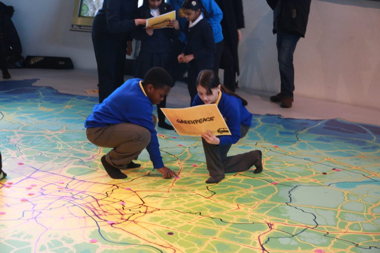 Two children crouch down on a giant floor map showing air pollution hotspots in London