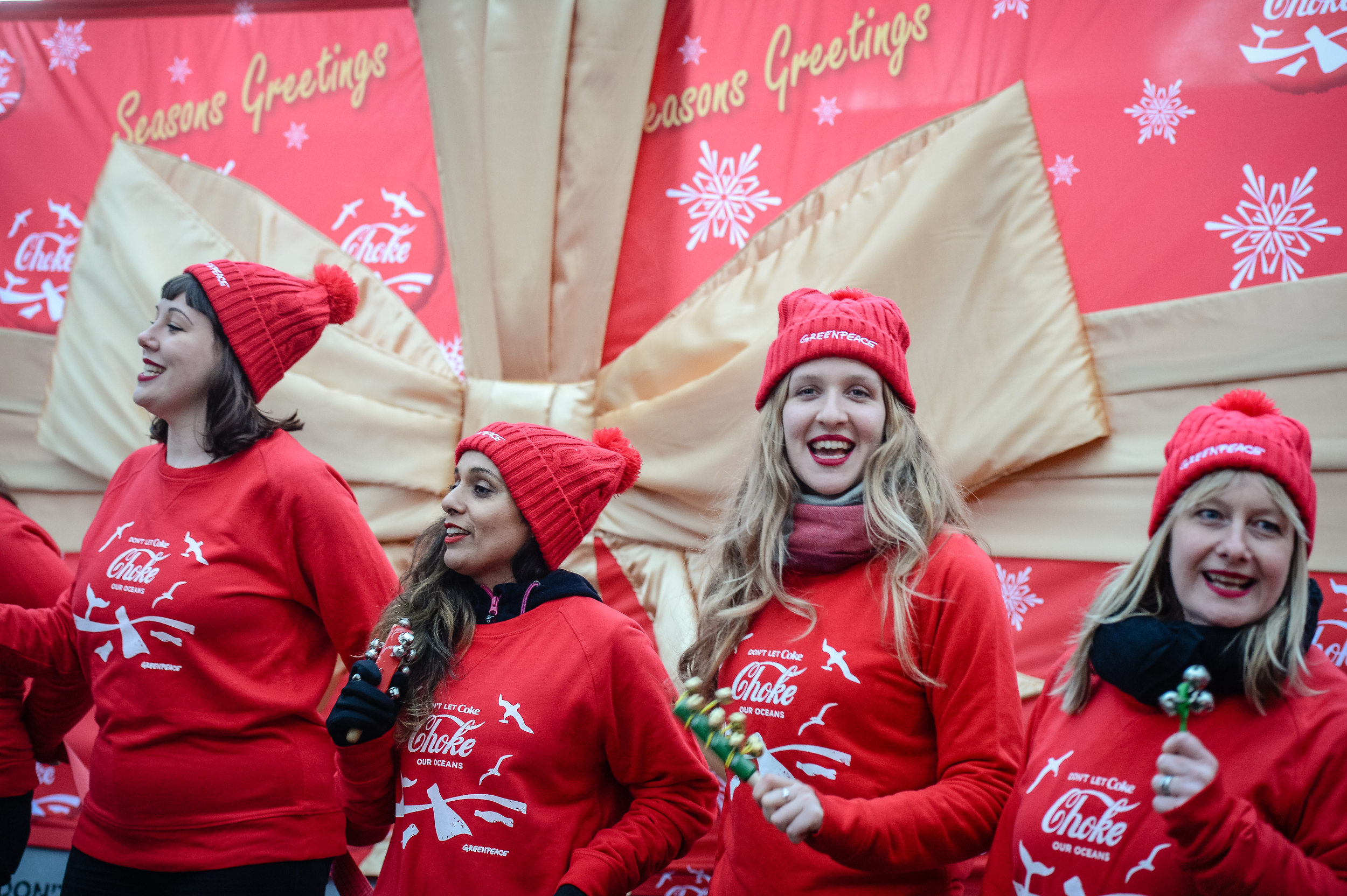 Meena with four white women dressed in red with 'Choke' Coca-Cola logo jumpers, in front of a huge red billboard logos