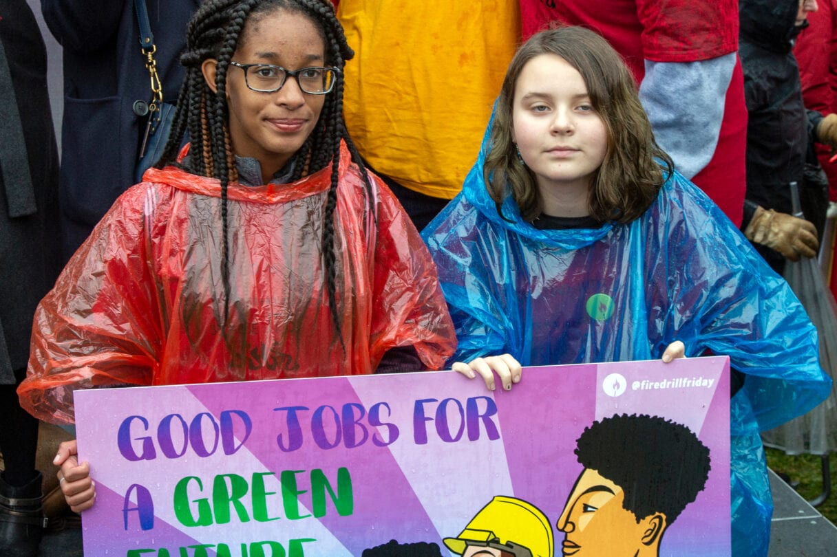 Two young protestors in plastic ponchos hold up a placard that says good jobs for a green future
