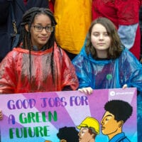 Two young protestors in plastic ponchos hold up a placard that says good jobs for a green future