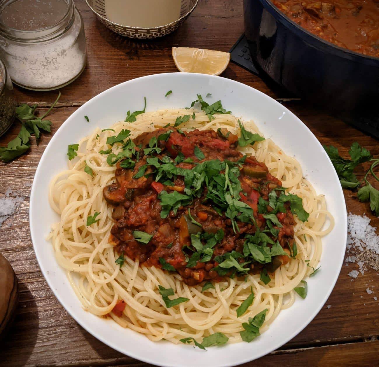 A plate of spaghetti with lentil bolognese, sprinkled with fresh herbs