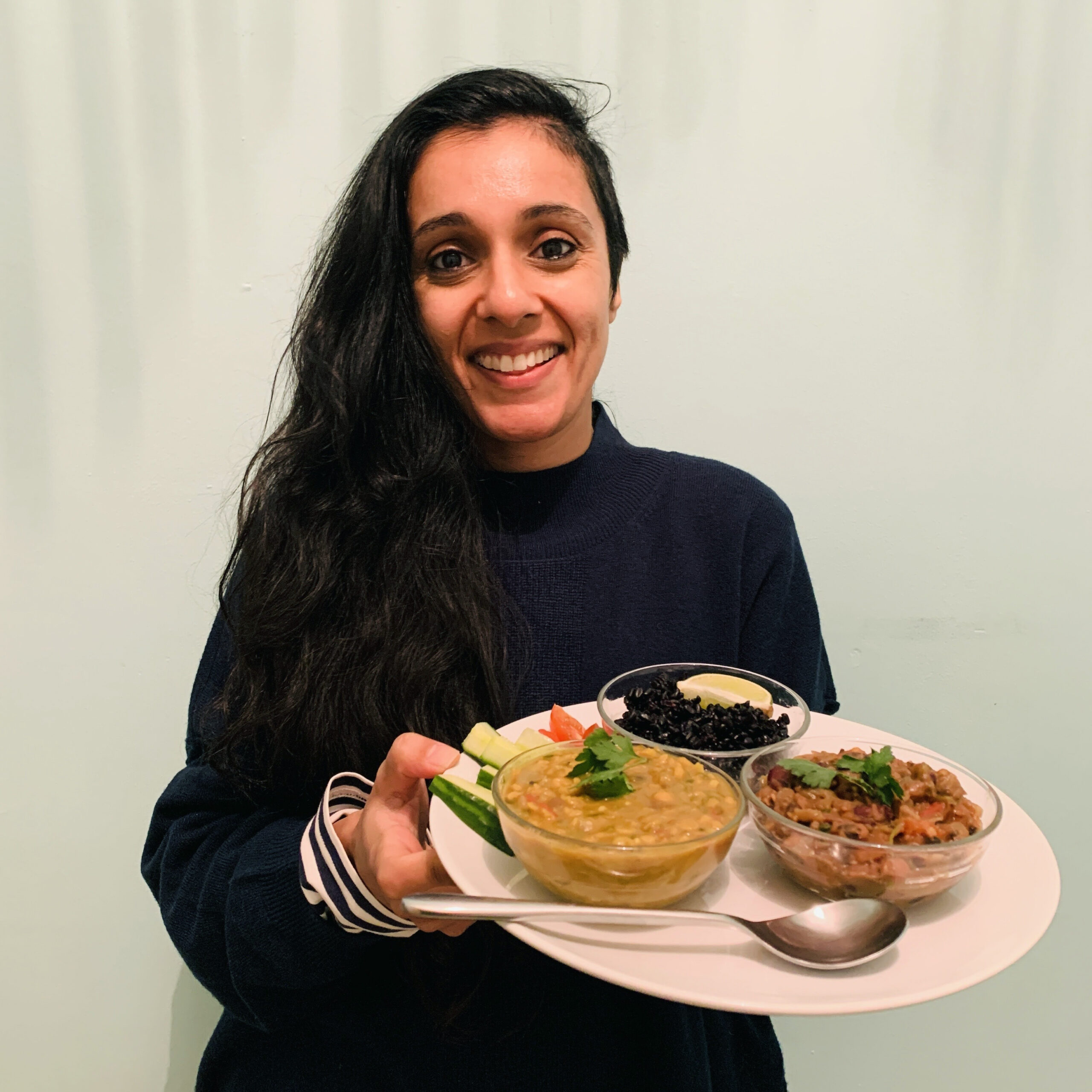 Meena holding a plate with three small bowls of different types of dahl