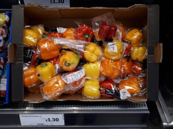 Plastic-wrapped red and yellow peppers on a supermarket display