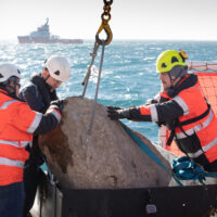 Greenpeace crewmembers prepare a boulder for placement on the seabed. A second ship is visible in the background