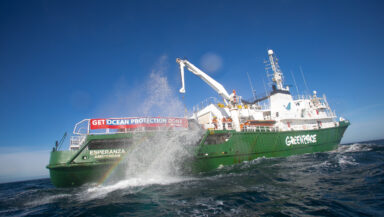 A large splash erupts alongside a Greenpeace ship as a boulder is placed in the water