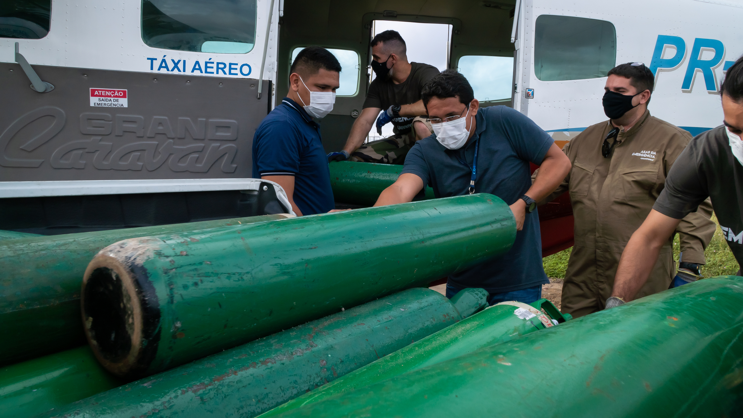 Three men with masks on loading an airplane taxi with long green oxygen tanks 