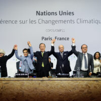 World leaders standing in a line and cheering in front of a United Nations conference backdrop during negotiations for the Paris Climate Agreement