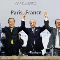World leaders standing in a line and cheering in front of a United Nations conference backdrop during negotiations for the Paris Climate Agreement