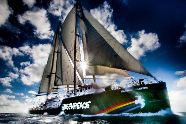 Sun shines through the sails of the Rainbow Warrior as it cuts through the ocean.