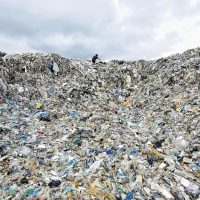 A worker stands at the top of a giant mound of plastic waste