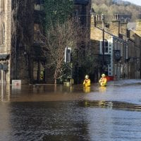 Rescue workers wade through a flooded street lined with old stone houses