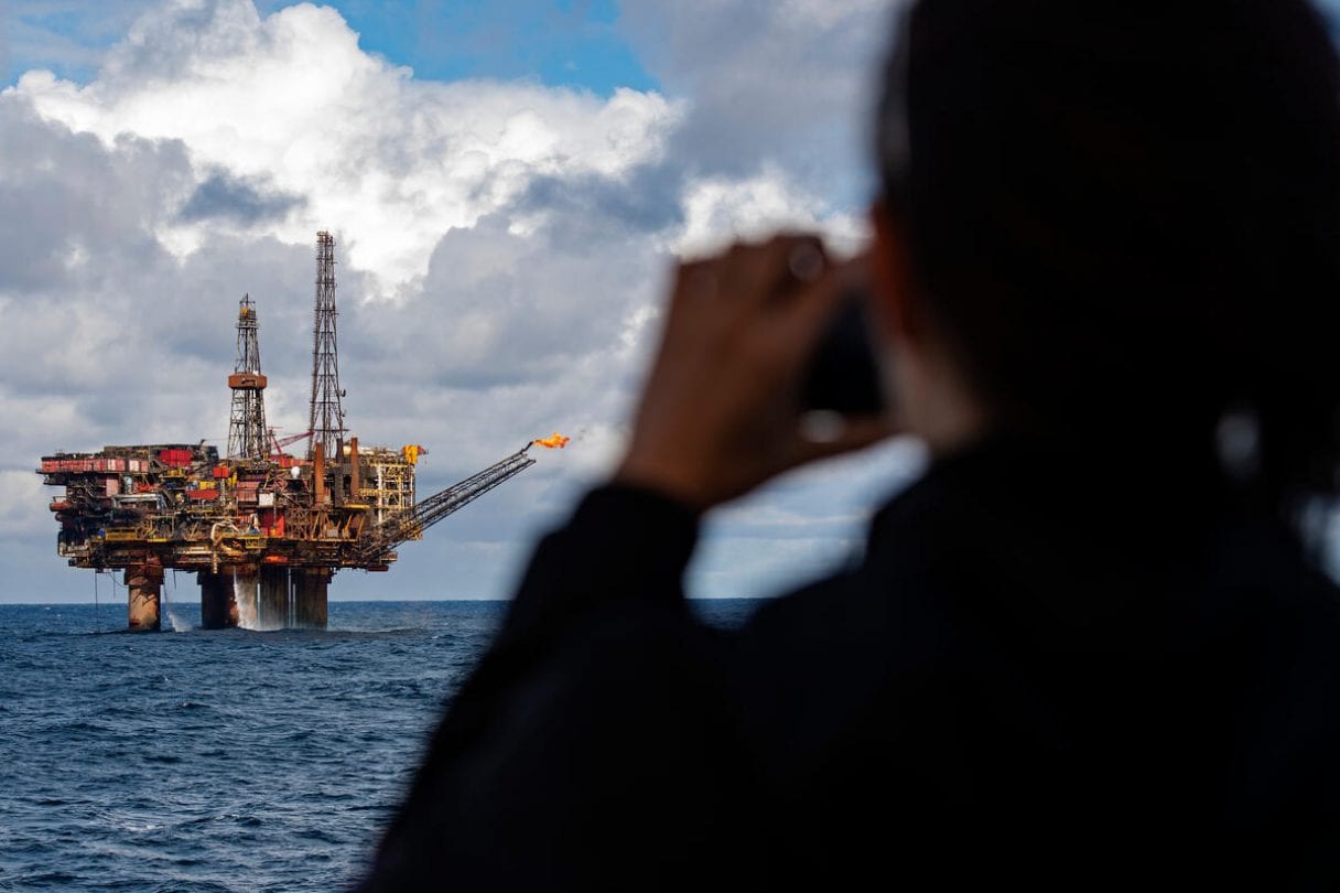 A person looks at a distant oil platform through binoculars.