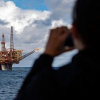 A person looks at a distant oil platform through binoculars.