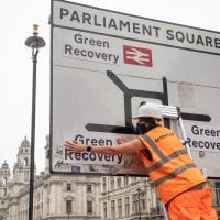 An activist replaces the destination names on a road sign in Parliament Square with labels saying 'Green Recovery'
