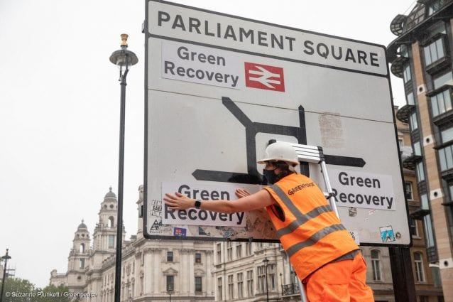 An activist replaces the destination names on a road sign in Parliament Square with labels saying 'Green Recovery'