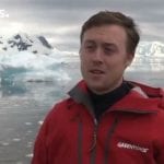 Portrait of Will McCallum in a red jacket with icy ocean behind.