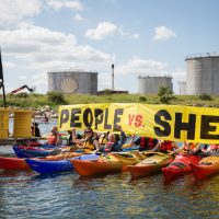 A row of people in colourful kayaks hold up a banner reading 'People vs Shell'