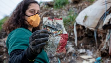 Greenpeace campaigner stands in a waste dump in Turkey, holding up a crisp packet from the UK
