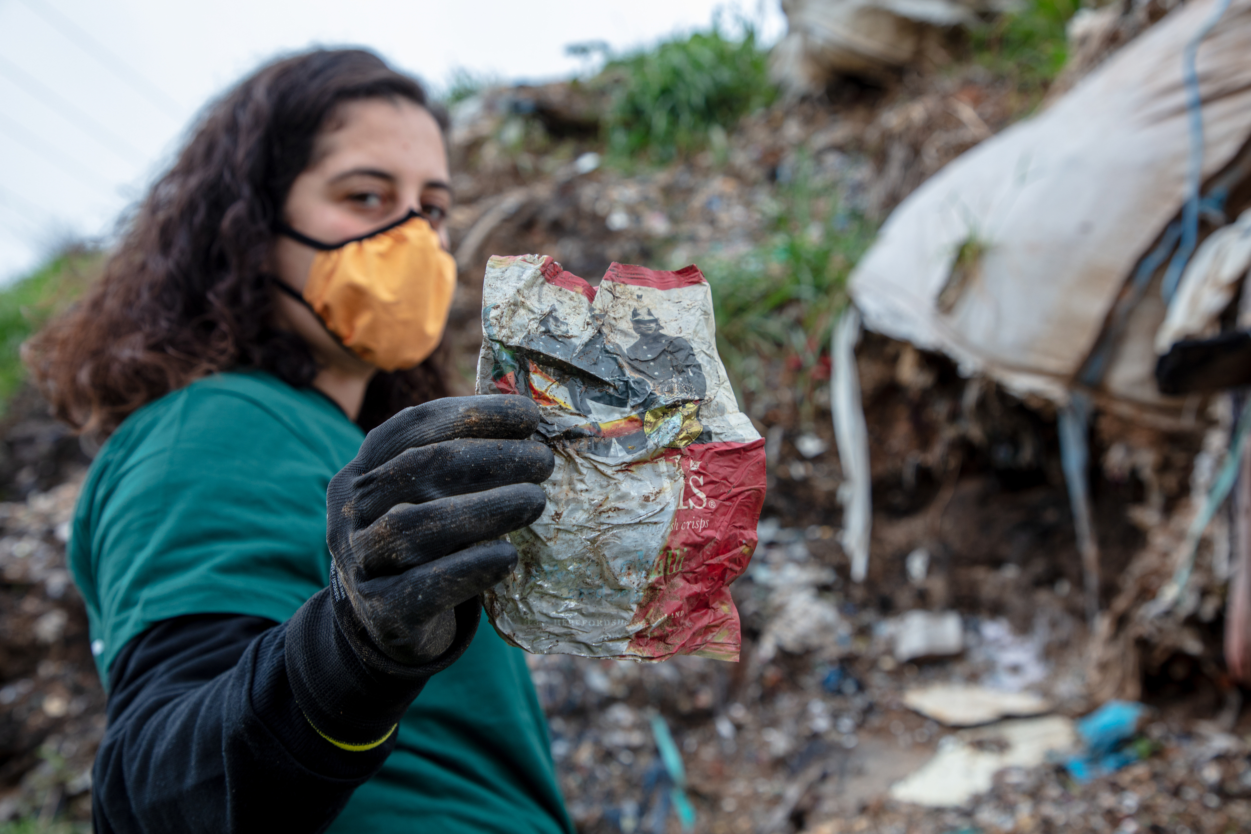 Greenpeace campaigner stands in a waste dump in Turkey, holding up a crisp packet from the UK