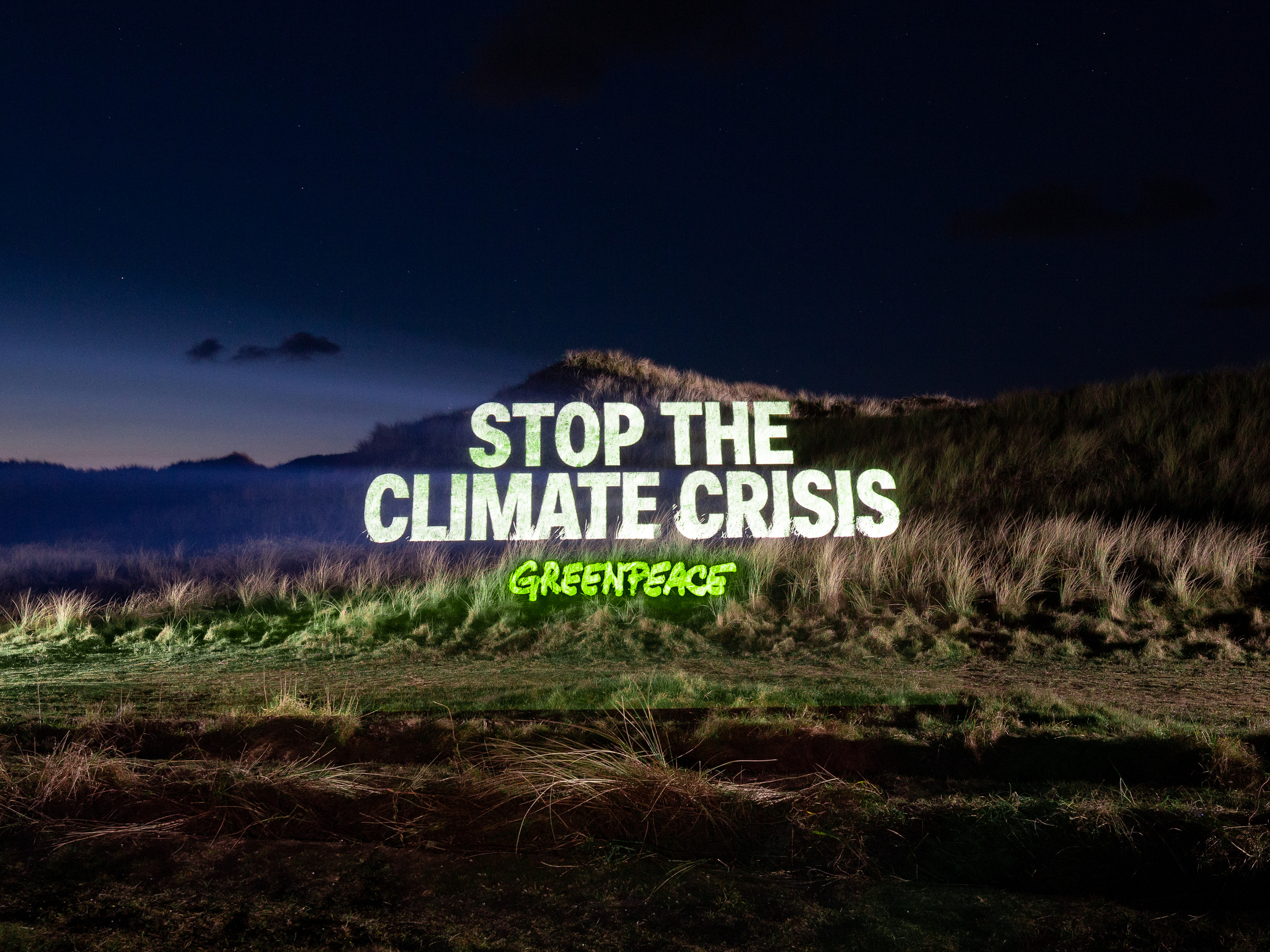A high-powered projector spells out the message "Stop the climate crisis" onto a beautiful night-time landscape