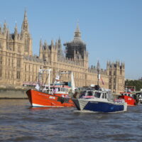 A group of small fishing boats sail alongside the UK's Houses of Parliament on the River Thames