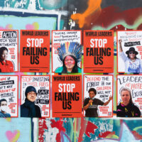 Posters featuring portraits of climate-impacted people from around the world are arranged in a grid on a graffiti covered wall outdoors. The portraits are interspersed with slogans and testimonials, with 'Stop failing us' appearing prominently.