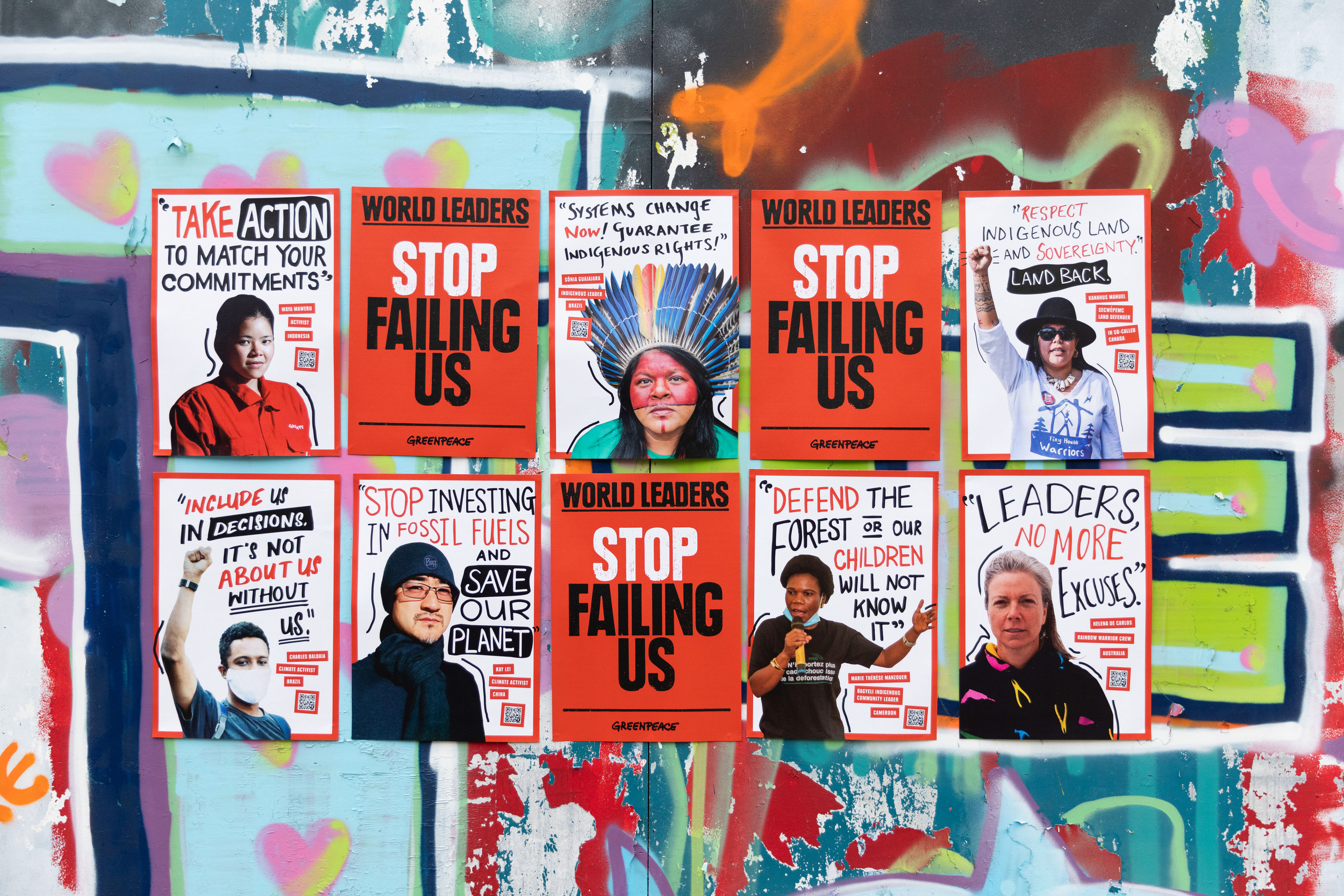 Posters featuring portraits of climate-impacted people from around the world are arranged in a grid on a graffiti covered wall outdoors. The portraits are interspersed with slogans and testimonials, with 'Stop failing us' appearing prominently.