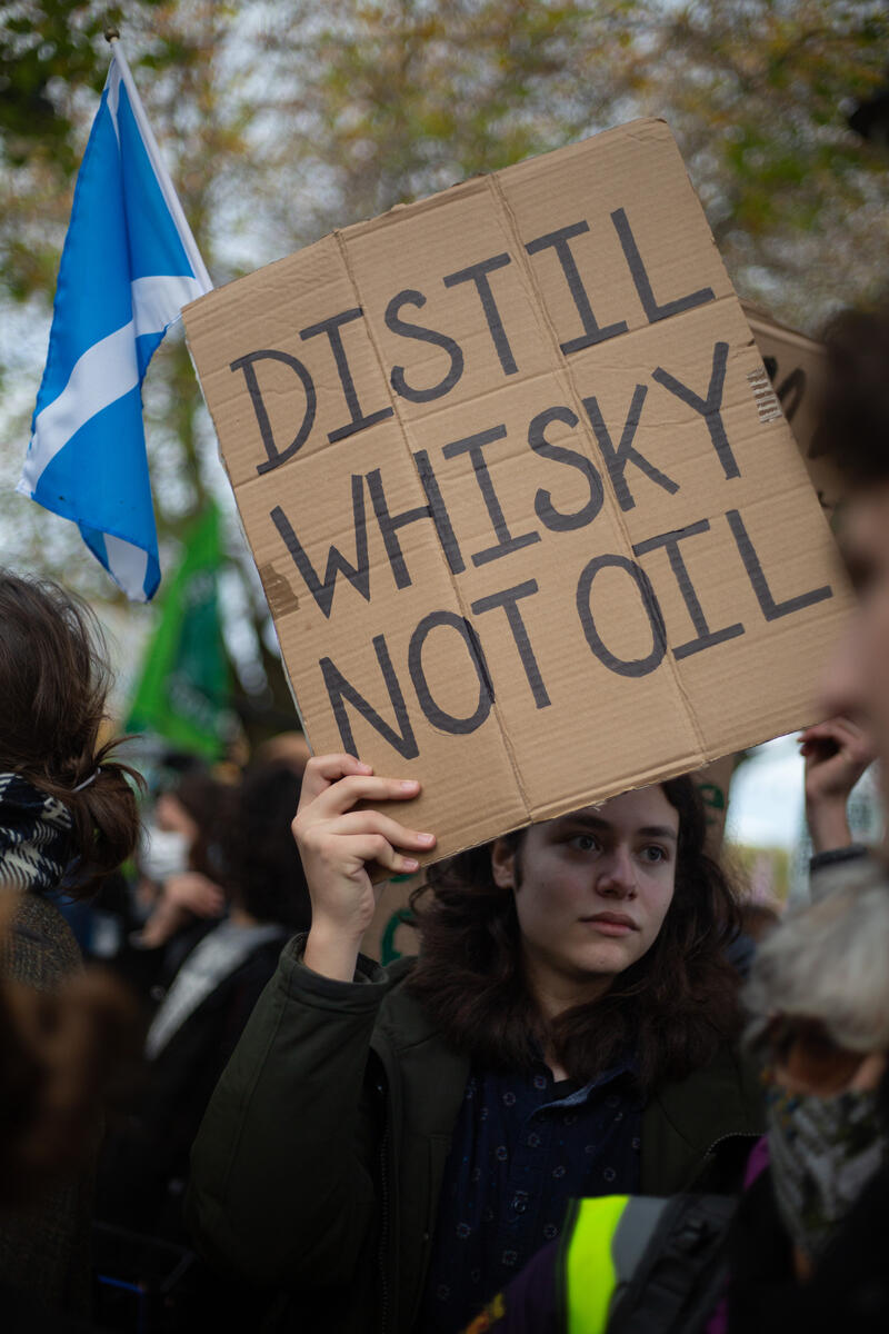 Climate marcher holds a sign saying 'Distil whisky not oil'