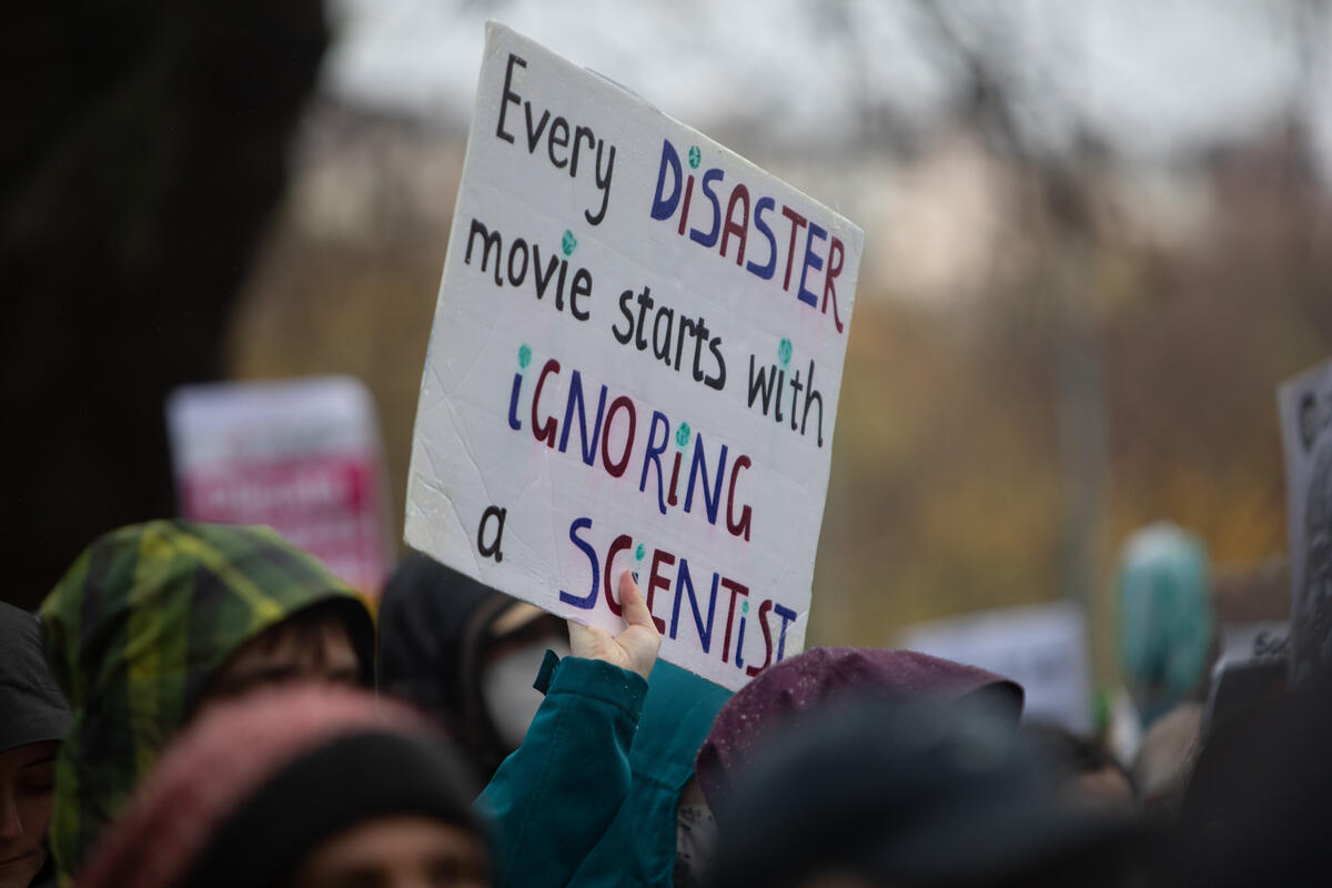 Climate marcher holds a sign saying 'Every disaster movie starts with ignoring a scientist'